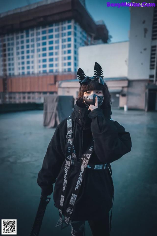 A woman wearing a black jacket and a cat mask.