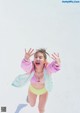 A woman in a pink jacket and yellow bikini jumping in the air.