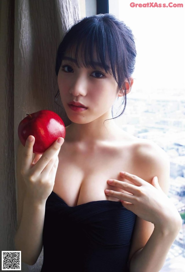 A woman in a black dress holding an apple.